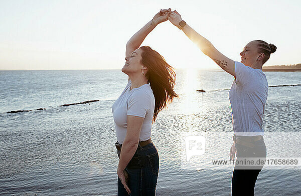 lesbian couple dancing together at the beach at sunset