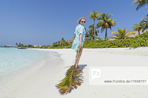 A woman walks along the beach with a palm branch.