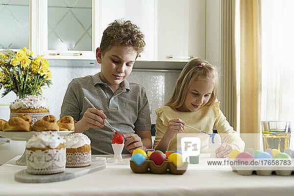 Brother and sister are painting Easter eggs.