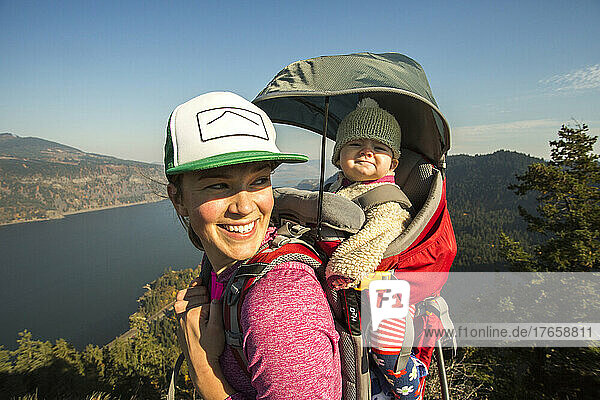 A young woman stands atop a mountain with a baby in a backpack