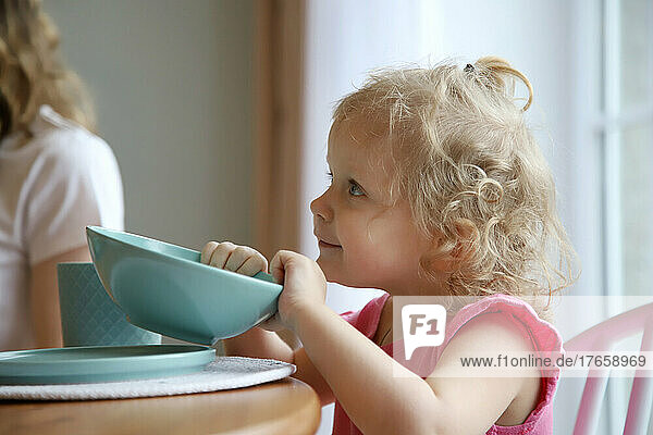 Baby sits at the table and holds a plate