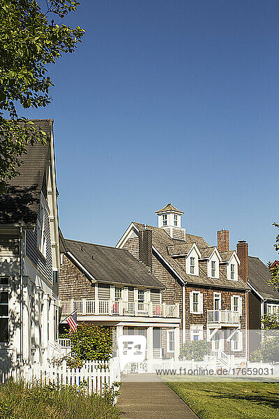 A row of shingled houses with white picket fences on a sunny day