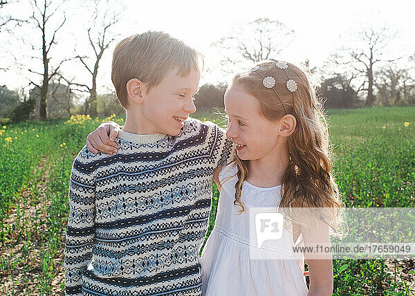 siblings hugging playfully in a field of flowers at sunset
