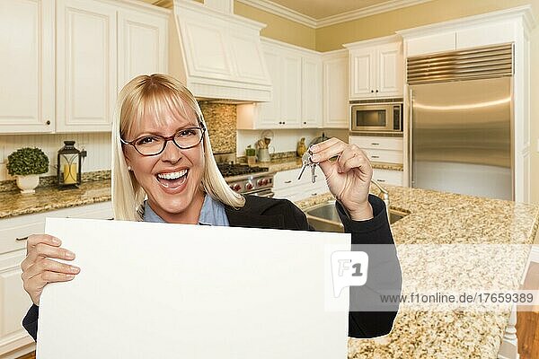 Glückliche junge Frau  die ein leeres Schild und Schlüssel in einer schönen individuellen Küche hält
