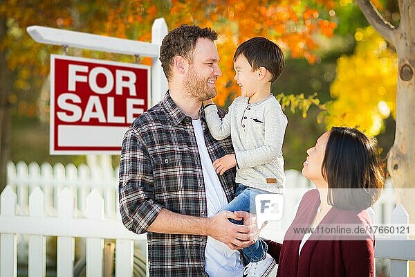 Gemischtrassige chinesische und kaukasische Eltern und Kind vor einem Zaun und einem Immobilienschild zum Verkauf