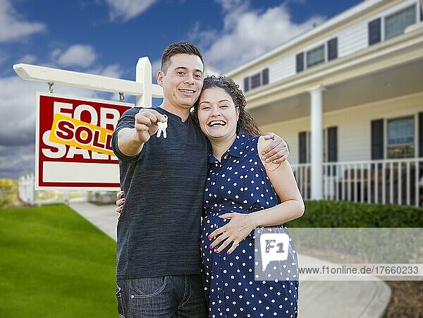 Happy hispanic couple in front of new home and sold real estate sign showing off their house keys