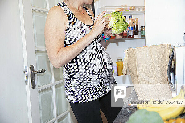Schwangere Frau räumt Lebensmittel in der Küche ein