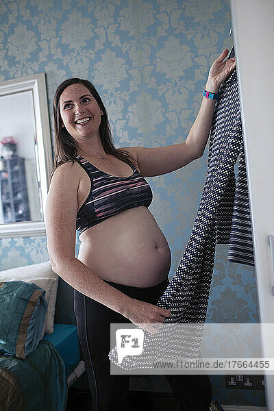 Smiling pregnant woman getting dressed in bedroom