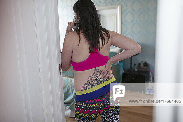 Pregnant woman in sports bra with tattoo talking on smart phone