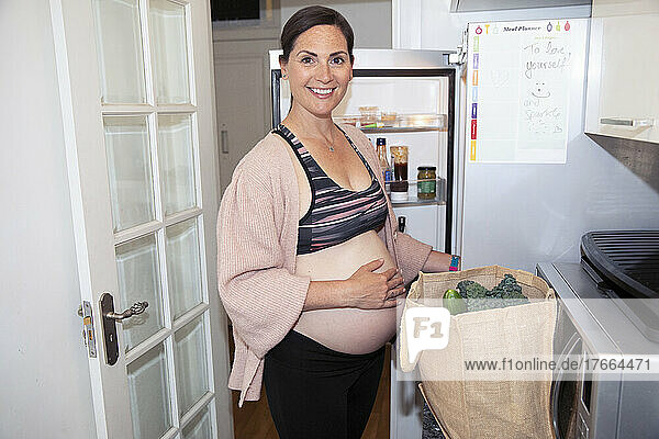 Portrait smiling pregnant woman in sports bra unloading groceries