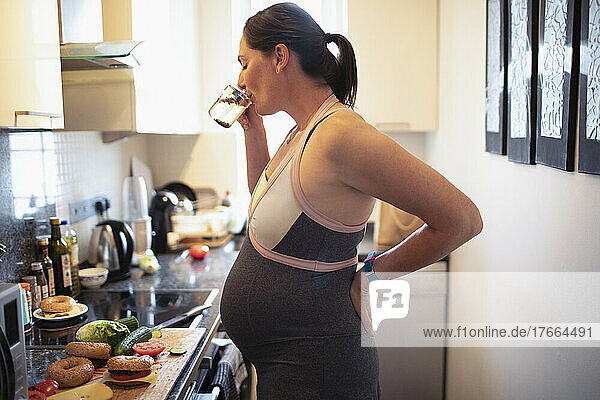 Schwangere Frau trinkt und isst in der Küche