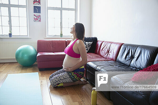 Gelassene schwangere Frau  die auf dem Boden ihres Wohnzimmers trainiert