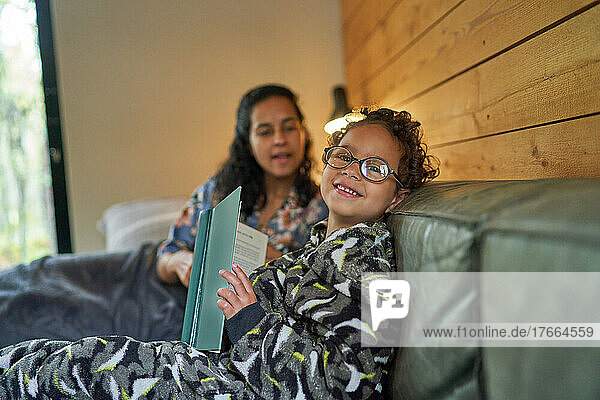 Porträt süßer Junge liest Buch mit Mutter auf Sofa