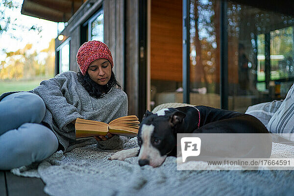 Eine Frau liest ein Buch neben ihrem Hund auf der Terrasse eines Ferienhauses