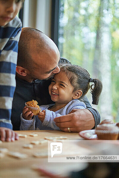 Vater umarmt glückliches Kleinkind Tochter essen Muffin am Tisch