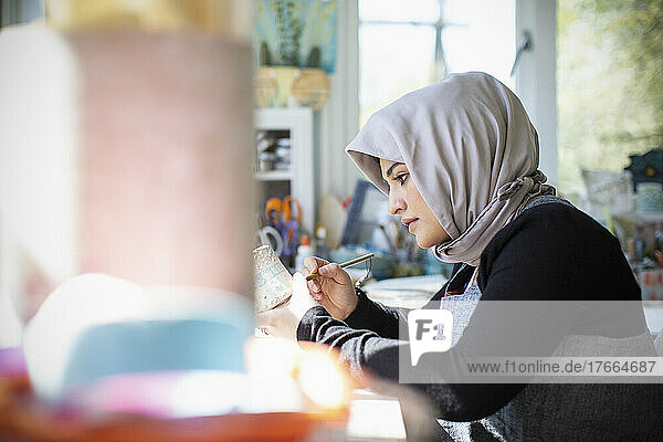 Fokussierte junge Künstlerin im Hidschab  die im Kunstatelier Keramik malt