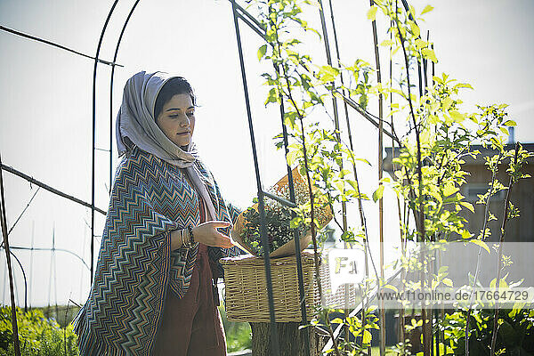 Junge muslimische Frau mit Blumen und Picknickkorb im sonnigen Garten