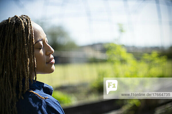 Gelassene junge Frau mit geschlossenen Augen im sonnigen Garten