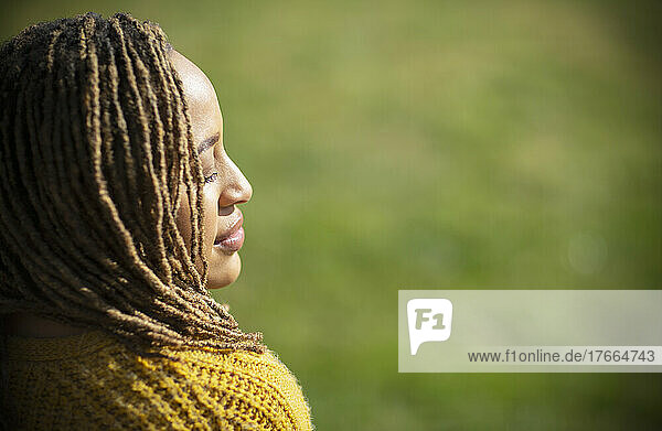 Gelassene junge Frau sonnt sich mit geschlossenen Augen im Sonnenlicht