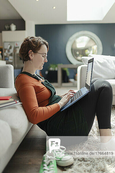 Junge Frau arbeitet von zu Hause aus am Laptop auf dem Wohnzimmerboden