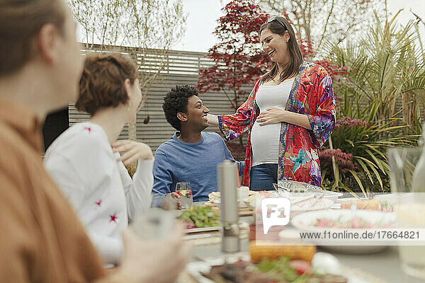 Glückliches schwangeres Paar genießt das Mittagessen mit Freunden am Terrassentisch