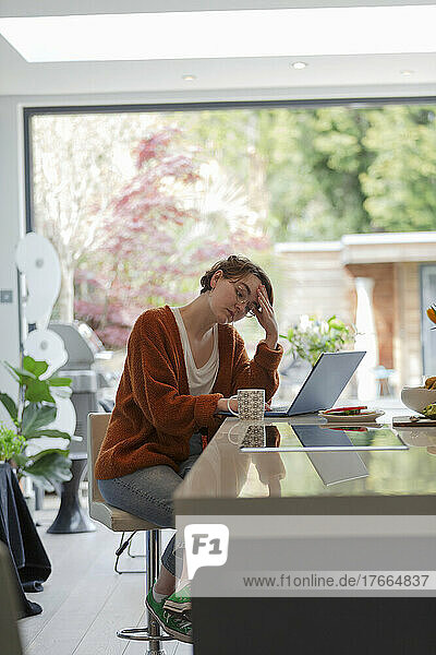 Stressed woman working from home at laptop in kitchen