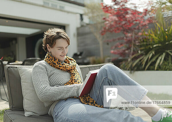 Junge Frau liest ein Buch auf einem sonnigen Liegestuhl auf der Terrasse