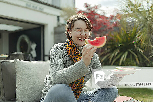 Glückliche junge Frau isst Wassermelone auf einer Sommerterrasse