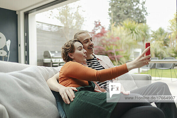 Verspieltes junges Paar macht Selfie mit Smartphone auf Sofa