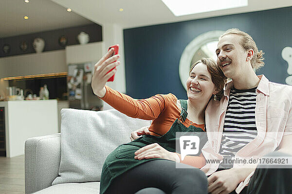 Happy young couple taking selfie on living room sofa