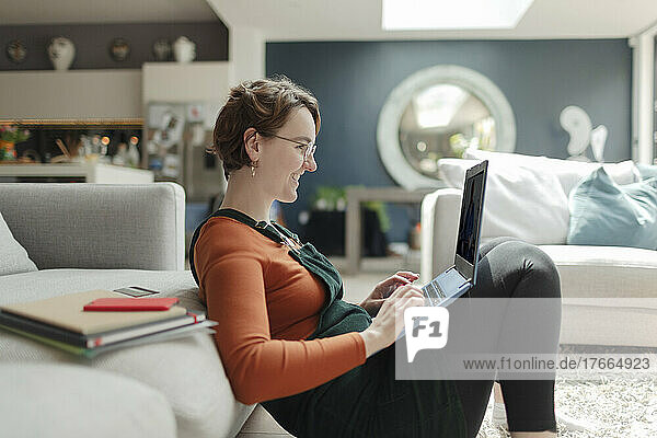 Junge Frau mit Laptop  die von zu Hause aus im Wohnzimmer arbeitet