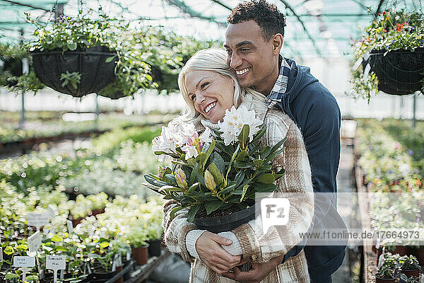 Glückliches Paar mit Topfblume  das sich im Gewächshaus umarmt
