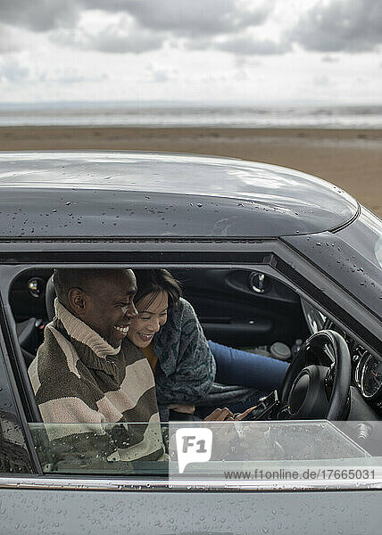 Glückliches Paar benutzt Smartphone im Auto am Winterstrand