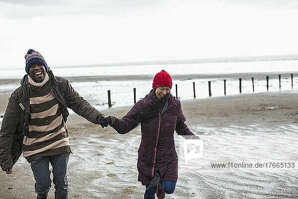 Happy carefree couple holding hands and running on wet winter beach