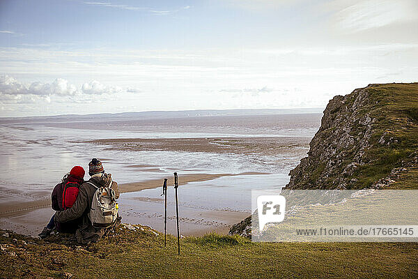 Wandererpaar  das auf einer Klippe über dem ruhigen Wintermeerstrand eine Pause einlegt