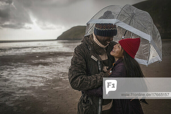 Glückliches Paar unter Regenschirm am nassen Winterstrand