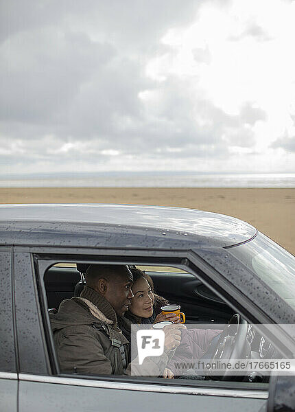 Happy couple drinking coffee in car on winter beach