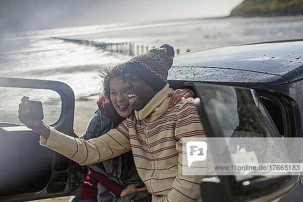 Glückliches verspieltes Paar macht Selfie im Auto am Winterstrand