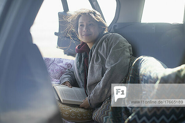 Gelassene Frau liest ein Buch auf dem Rücksitz eines Autos