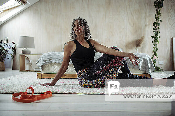 Senior woman practicing yoga twist on bedroom floor