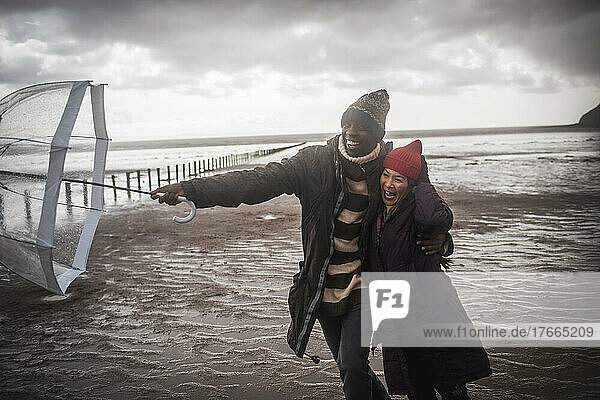 Verliebtes Paar mit Regenschirm am nassen Winterstrand