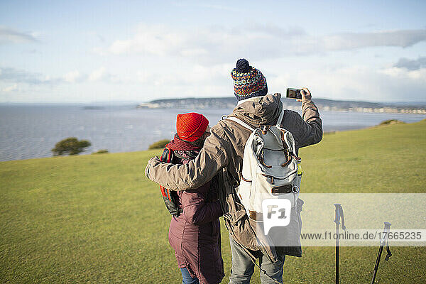 Hiker couple with camera phone on cliff with sunny ocean view