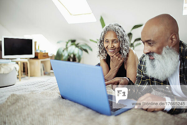 Happy senior couple using laptop on bed