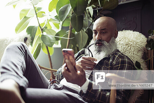 Älterer Mann mit Bart benutzt Smartphone im Sessel