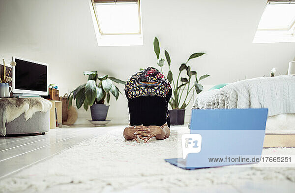 Frau übt Yoga online mit Laptop auf dem Schlafzimmerteppich