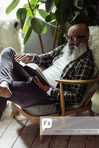 Älterer Mann mit Bart liest Buch im Sessel