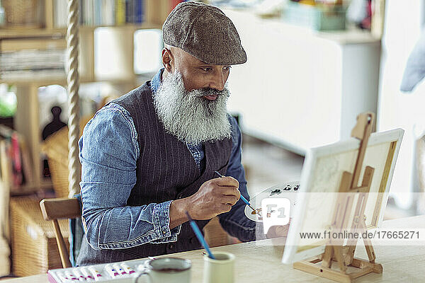 Älterer Mann mit Bart malt an Staffelei