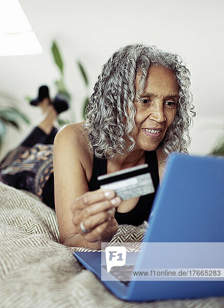 Ältere Frau mit Kreditkarte beim Online-Shopping am Laptop