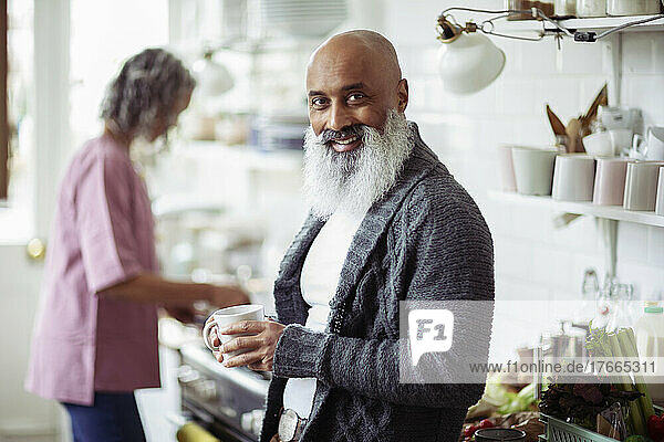 Portrait glücklicher reifer Mann mit Bart trinkt Kaffee in der Küche