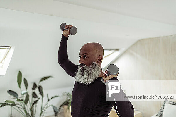Älterer Mann mit Bart trainiert mit Hanteln zu Hause